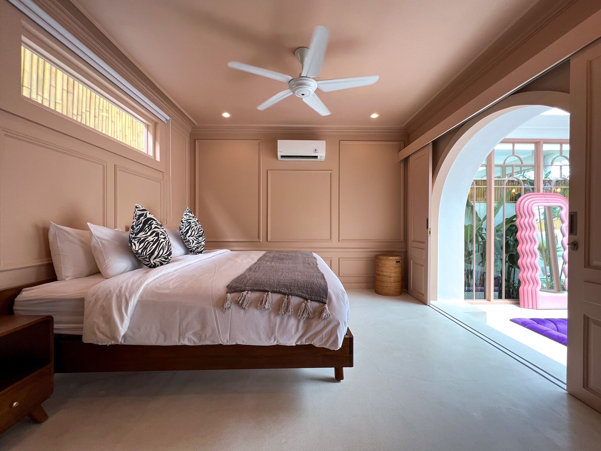 A bedroom with a bed, a ceiling fan, a window, and a door leading to a balcony.