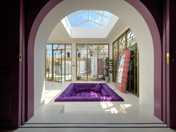 A modern interior with a purple sectional sofa, large glass doors leading to an outdoor area, and a skylight above.