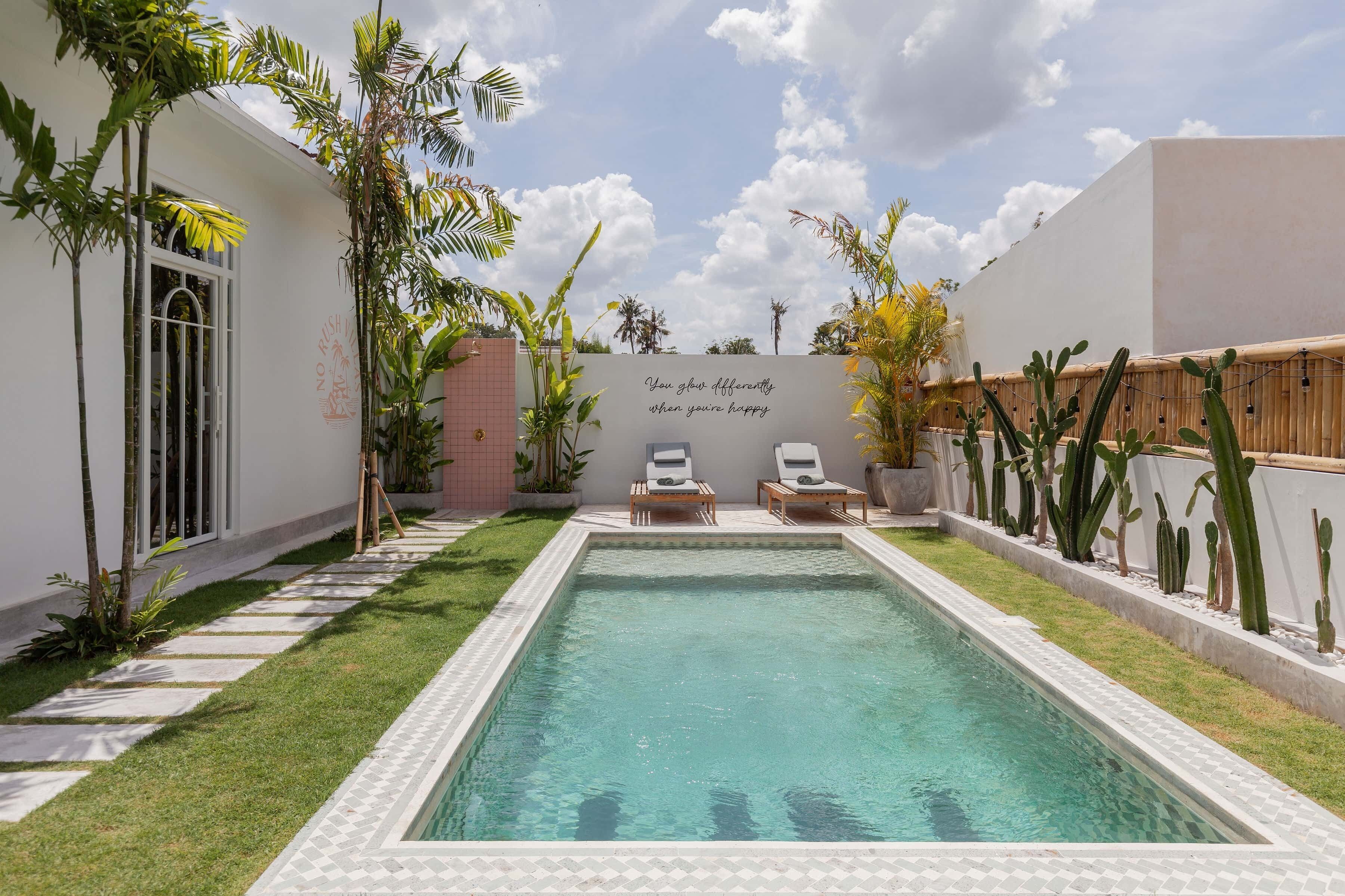 A swimming pool with two lounge chairs, surrounded by a garden with various plants and a wall with a motivational quote.