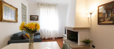 A living room with a white table, a vase with yellow flowers, a sofa, a fireplace, and a painting on the wall.