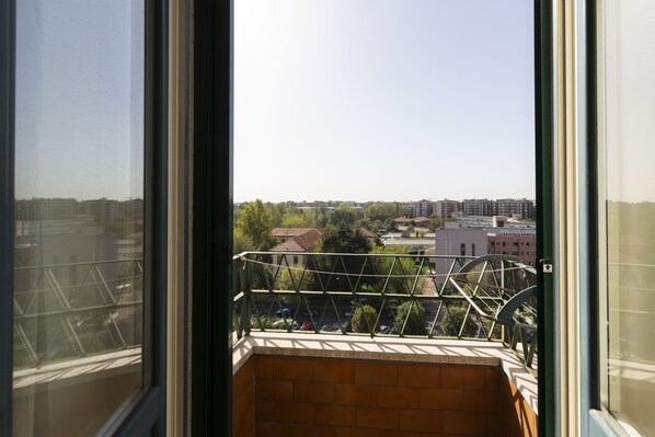 Une vue depuis un balcon doté d’une rambarde en métal, donnant sur un paysage urbain comprenant des bâtiments et des arbres.