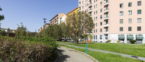 Un chemin bordé de verdure et d’immeubles dotés de balcons, sous un ciel dégagé.