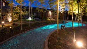 A nighttime pool area with a curved edge, surrounded by bamboo trees and a building with a brick facade. - yumotoankiyohime (Kirishima)