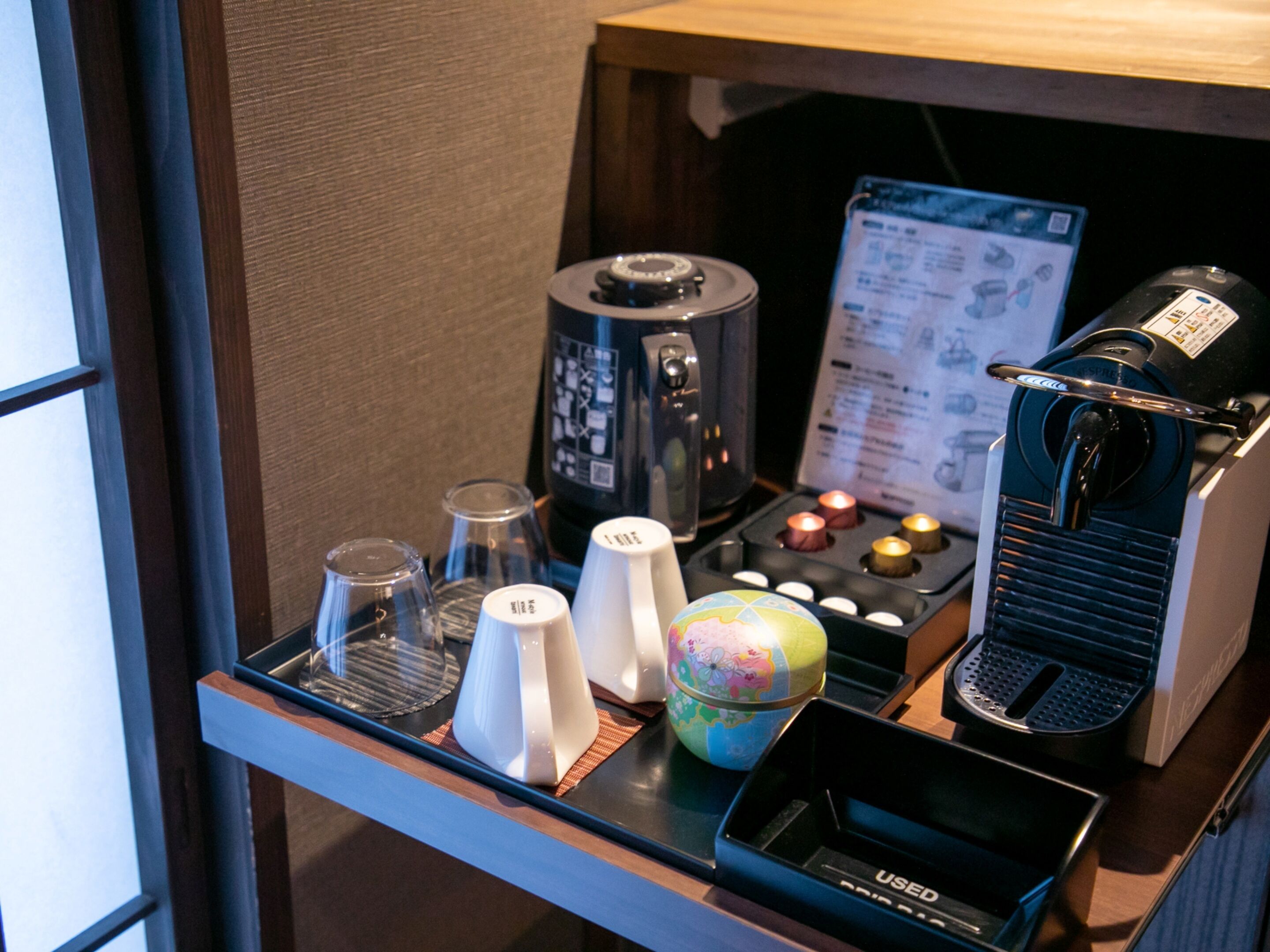 Un minibar con cafetera, tetera, vasos y un pequeño globo terráqueo.