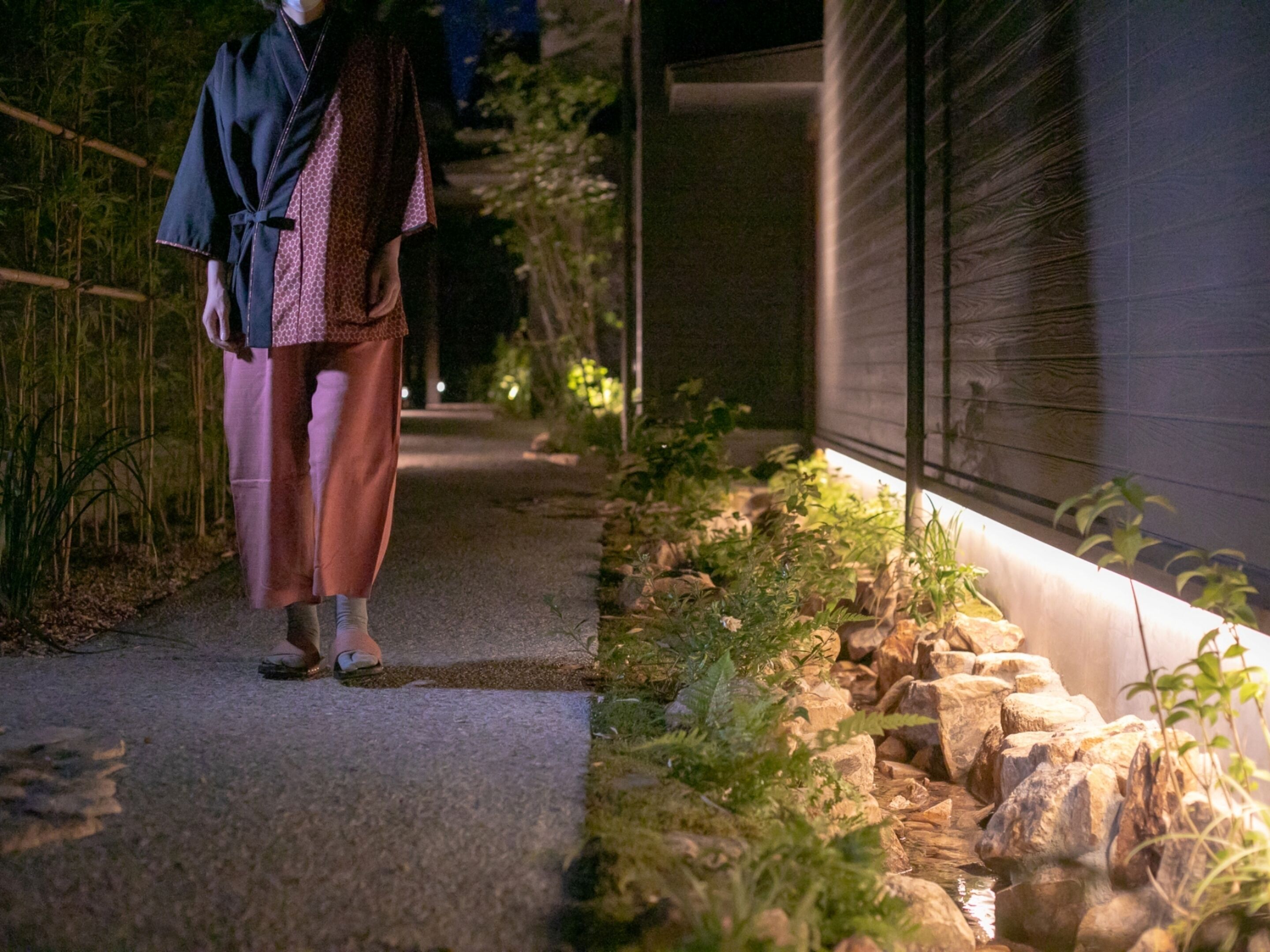 A pathway leading to a building with a rock garden and bamboo.