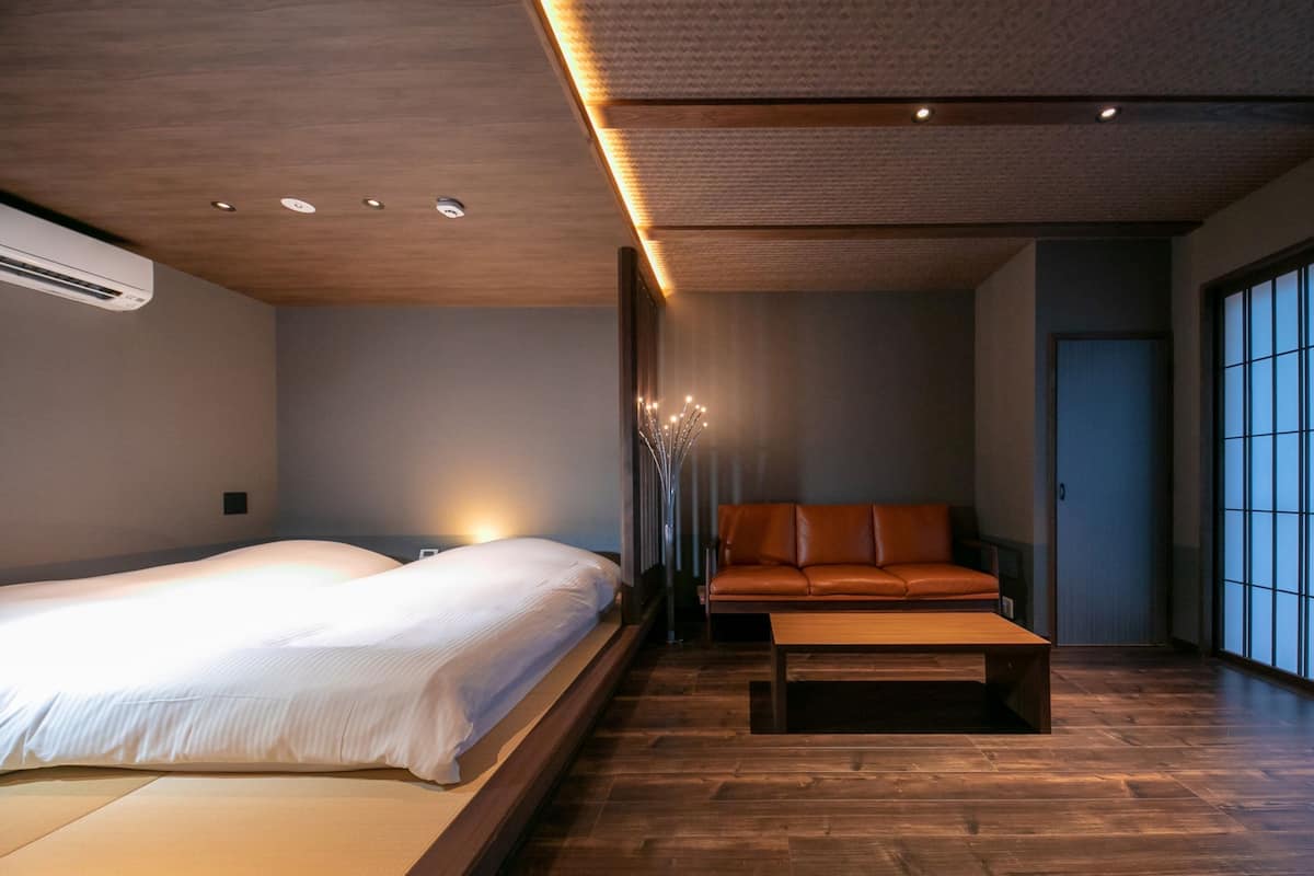 Quarto moderno com uma cama grande, um banquinho de madeira e um sofá.