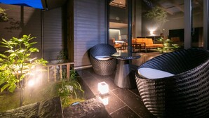 A modern outdoor seating area with wicker furniture and a glass wall overlooking a garden. - yumotoankiyohime (Kirishima)