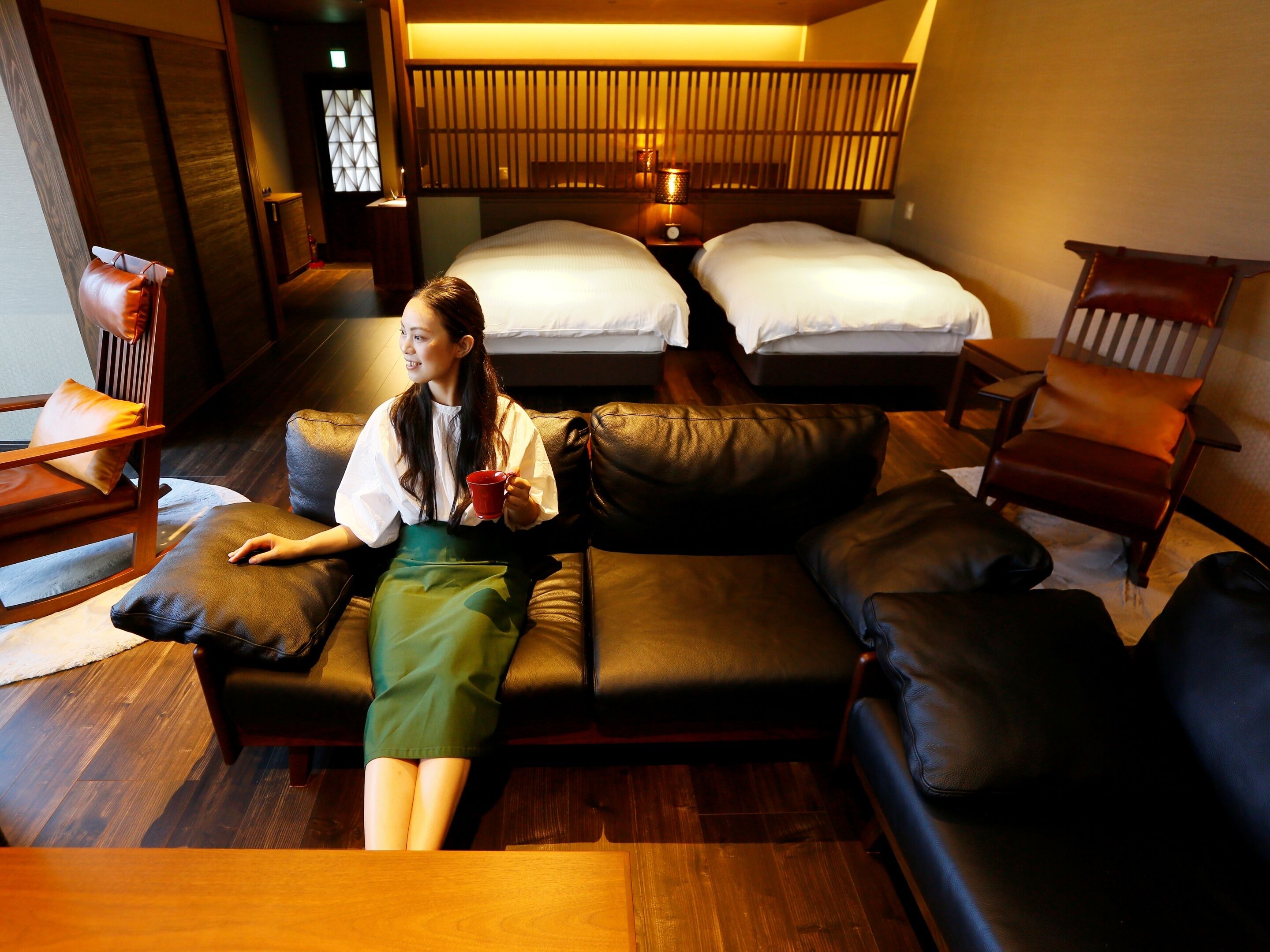 A room with a sofa, two beds, a wooden partition, and a small table.