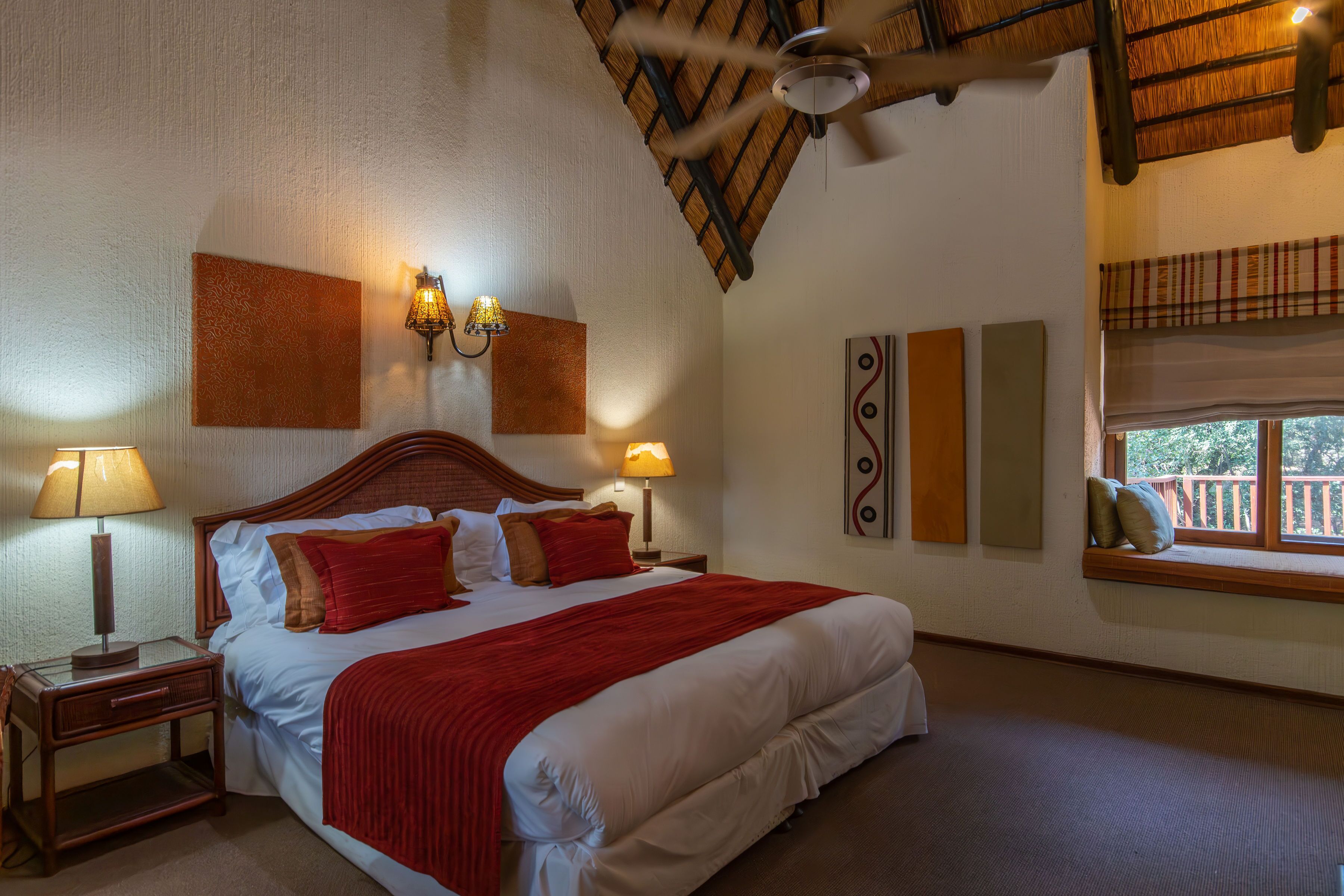 A hotel room with a large bed, two bedside lamps, a ceiling fan, and a window with a view.