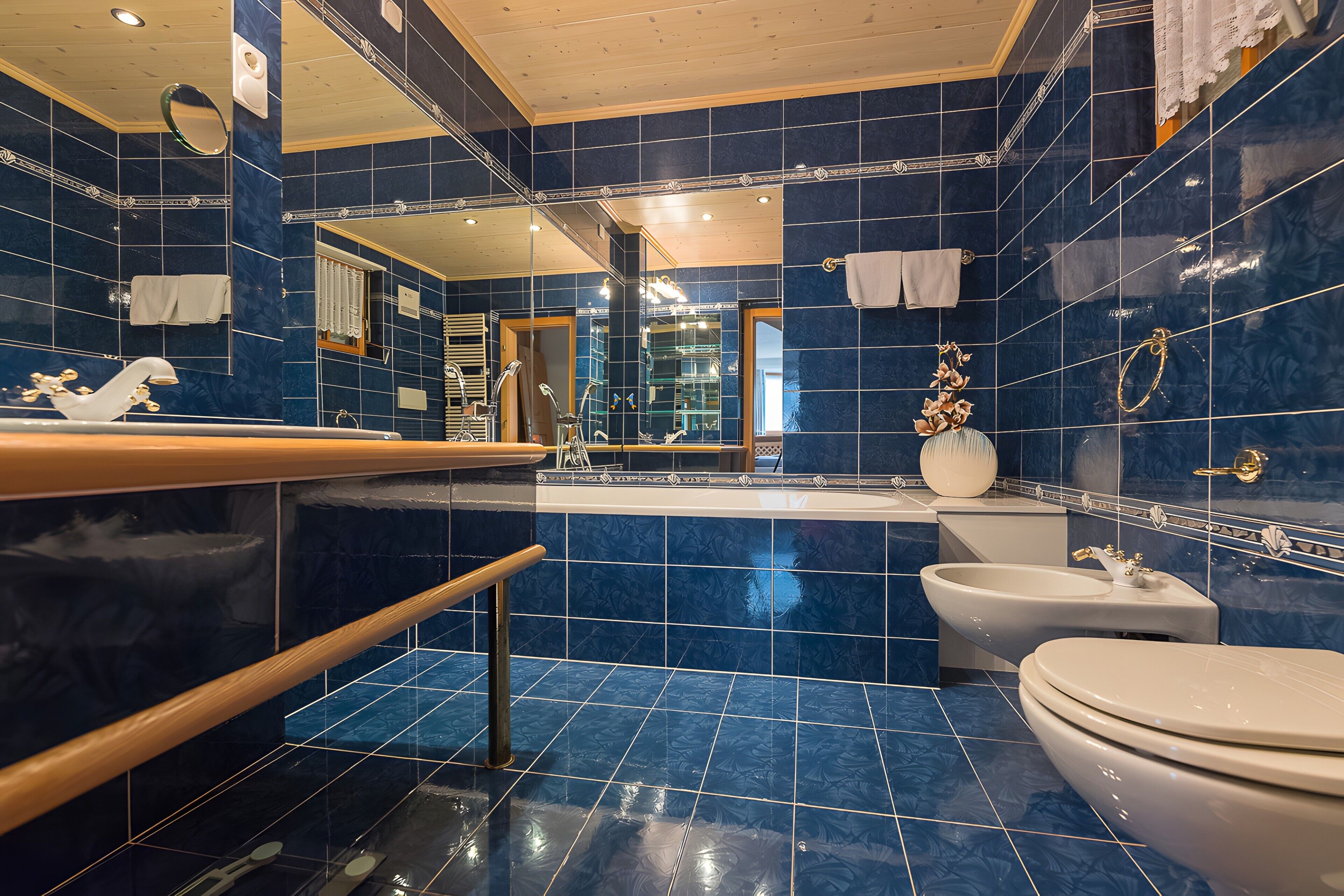 A bathroom with a bathtub, toilet, and sink, featuring blue tiles and a wooden vanity.