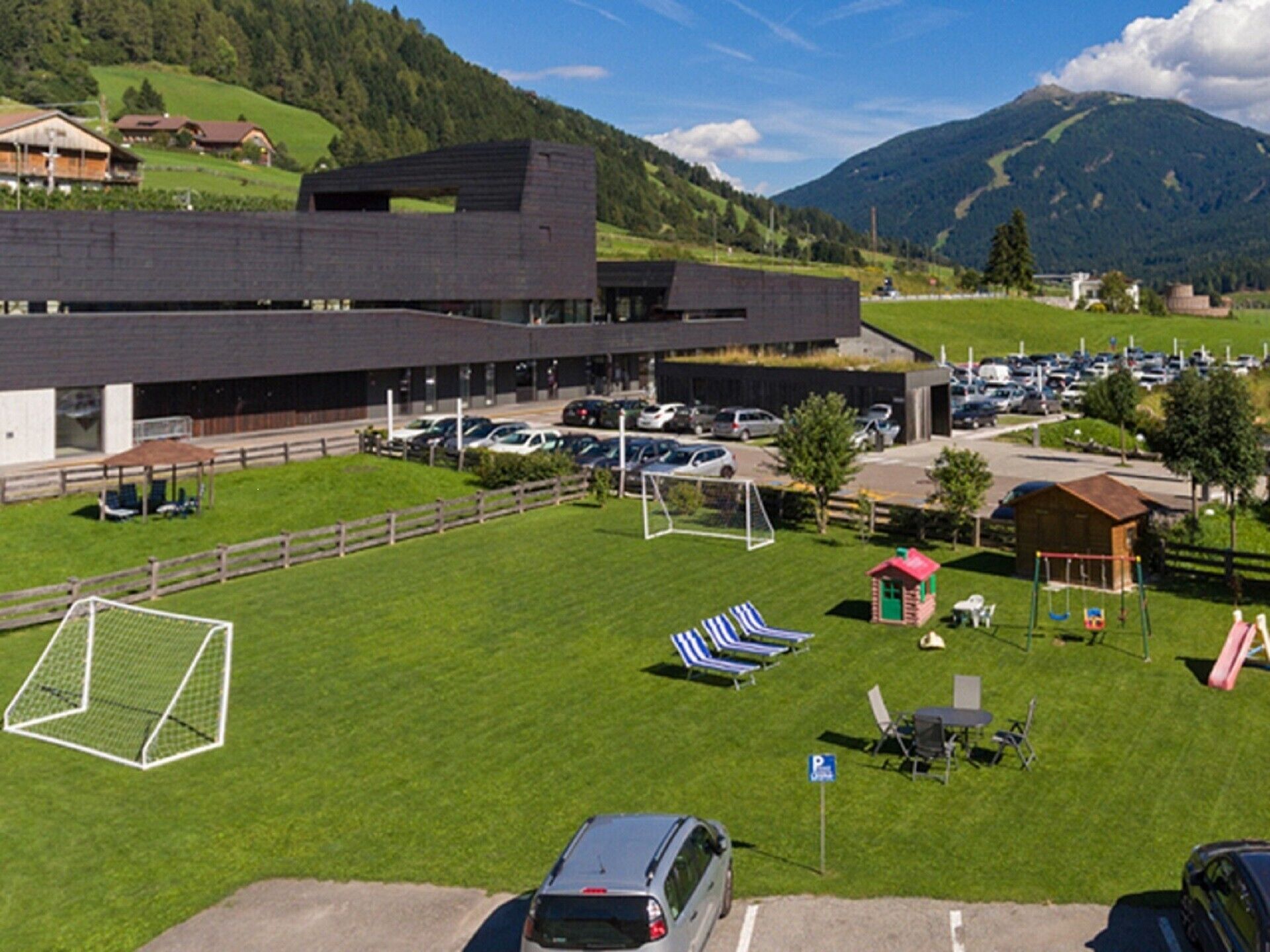 Un parcheggio con un edificio moderno, un campo da calcio e un'area giochi.