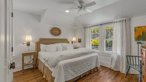 Un dormitorio con cama, lámparas de noche, ventilador de techo, ventana con cortinas y cómoda.