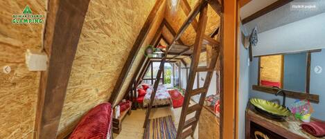 A narrow attic bedroom with a wooden ceiling, a small window, and a view of the outdoors.