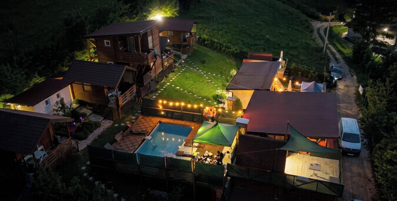 A multi-story wooden building with a swimming pool, a tennis court, and a covered patio area.