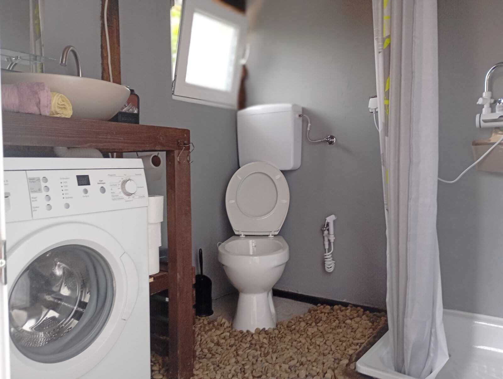 A compact bathroom with a washing machine, toilet, and shower area.
