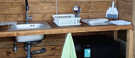 A compact wooden cabin with a sink, a small refrigerator, and a bench.