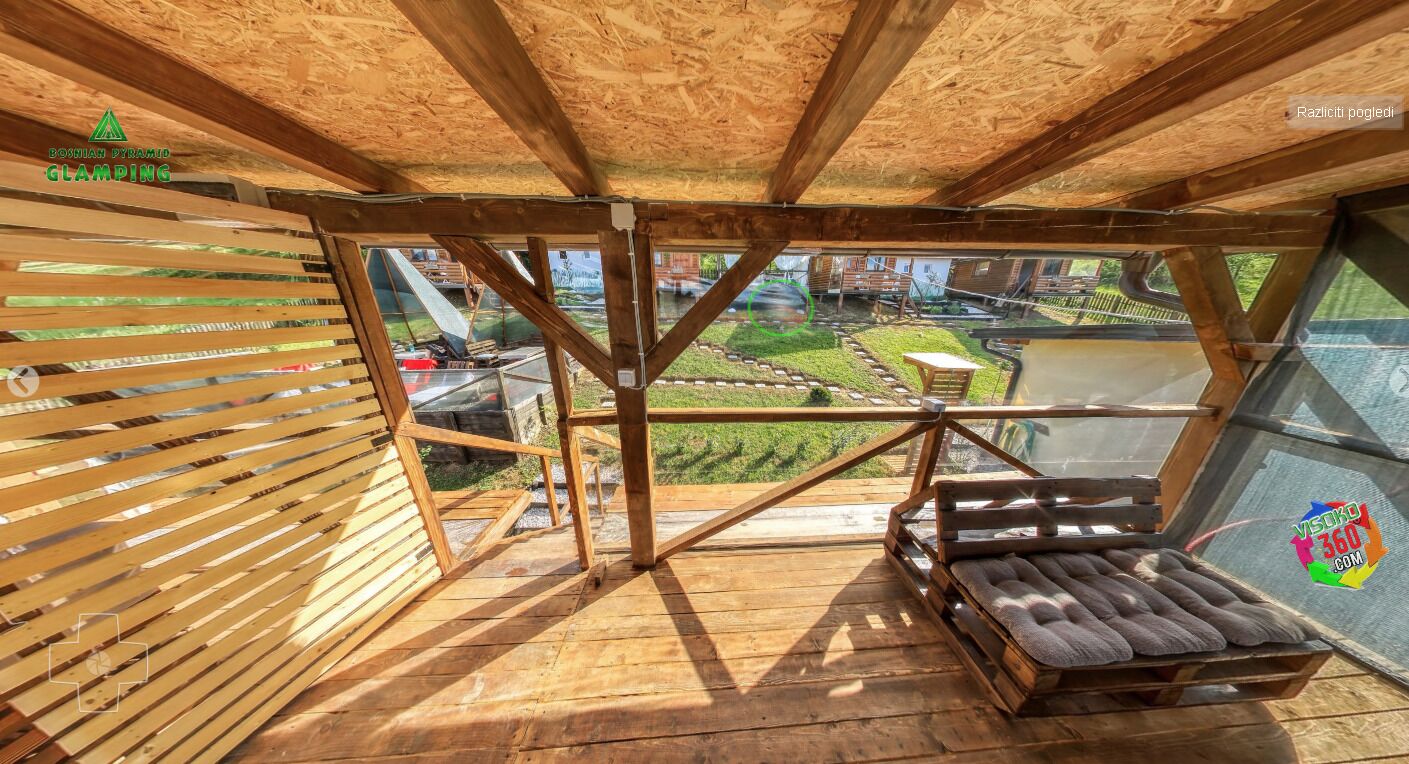 A wooden deck with a glass railing overlooking a garden.