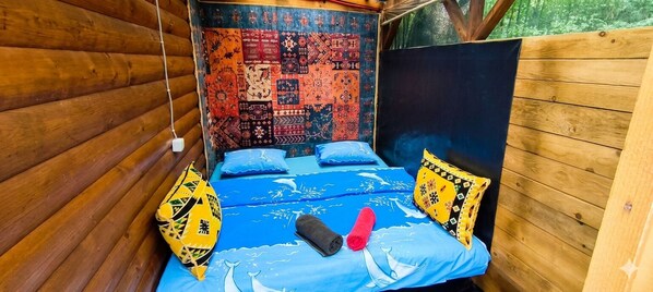 Quarto de cabana de madeira com cama, tapeçaria de parede estampada e vista para o verde lá fora.