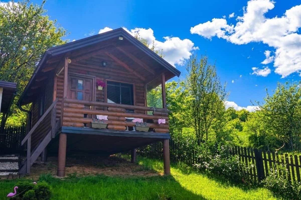 Eine Holzhütte mit Balkon, umgeben von üppigem Grün und blauem Himmel.