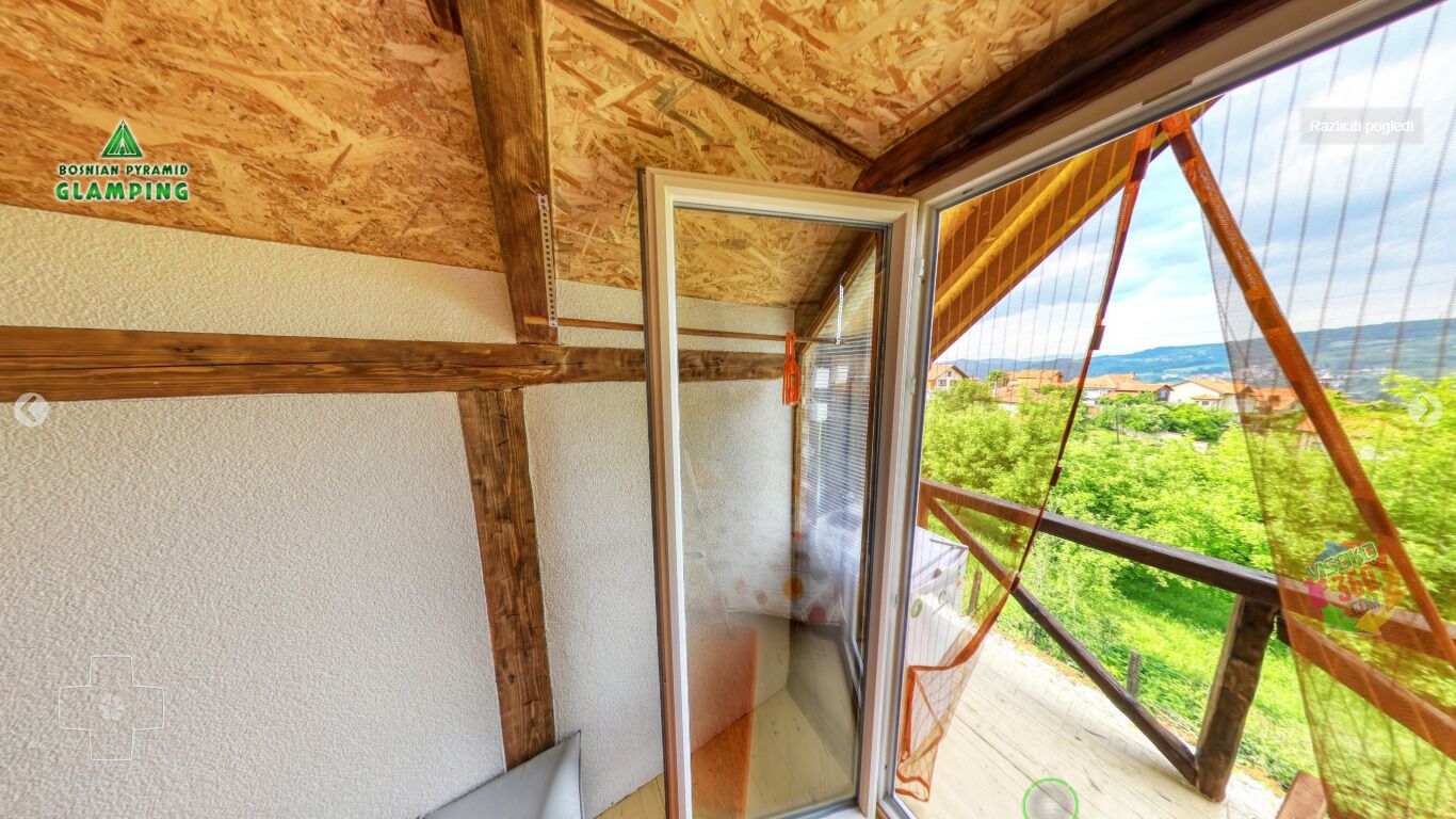 Une pièce avec un plafond en bois, une porte vitrée donnant sur l’extérieur et une vue sur la verdure et les bâtiments.