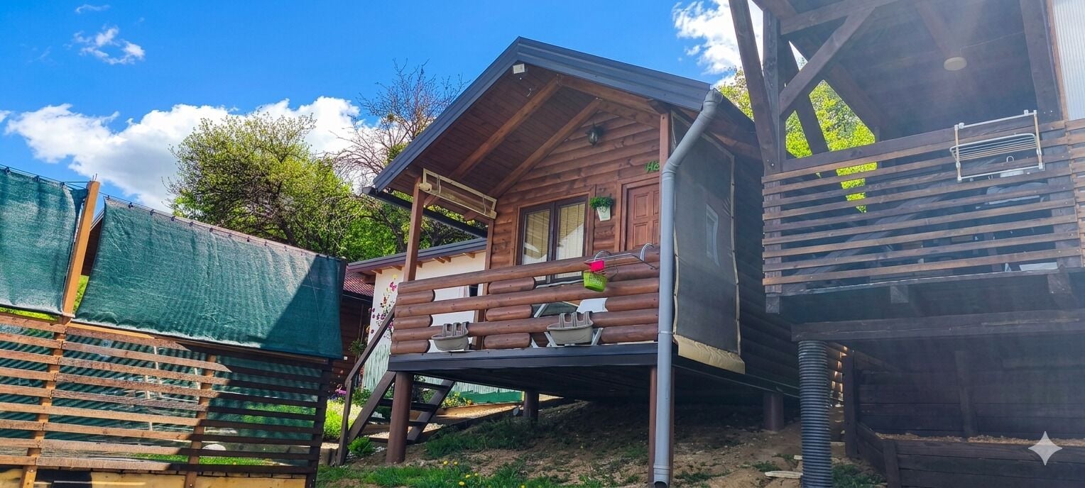 Eine Holzhütte mit Balkon, einer kleinen Veranda und einem Fenster mit einer Pflanze.