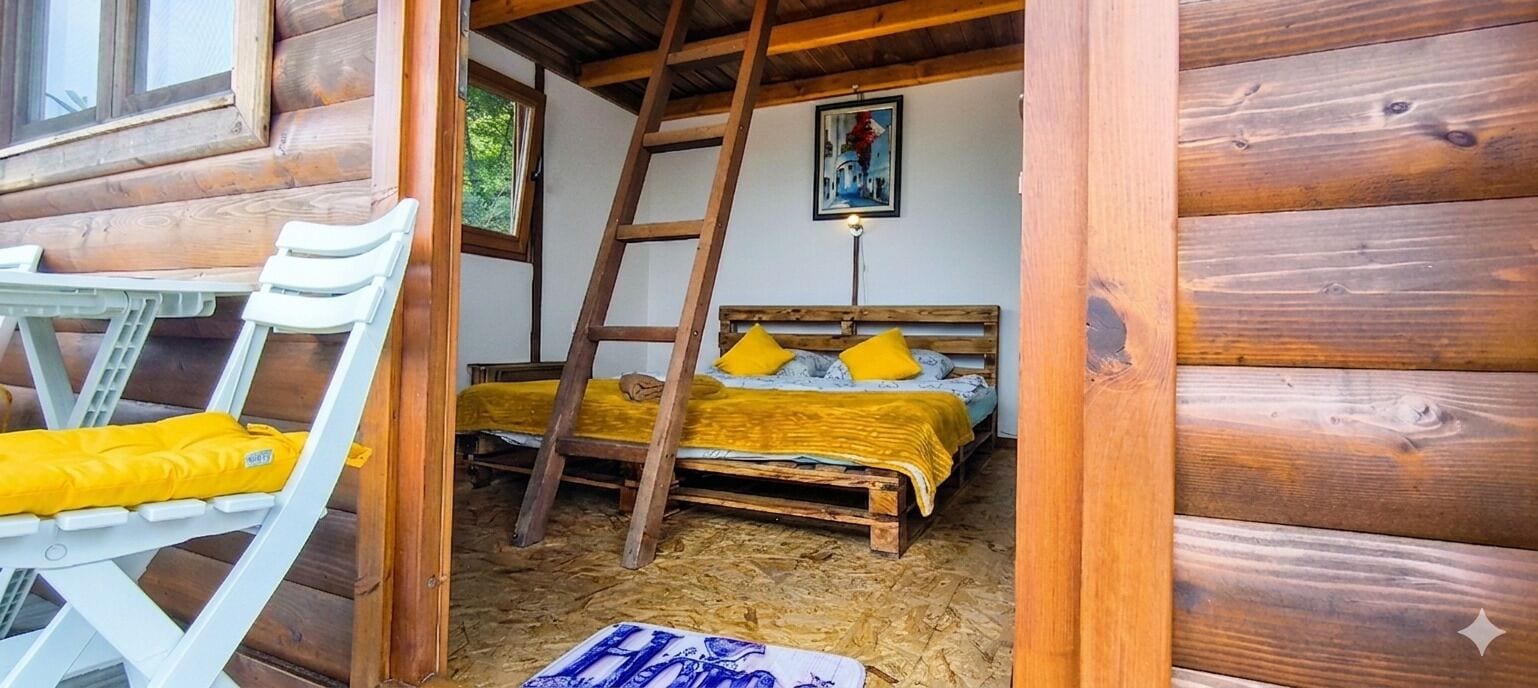 A wooden cabin interior with a bed, a ladder, and a white chair with a yellow cushion.