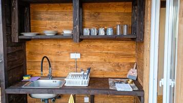 A wooden cabin kitchen with a sink, shelves with dishes, and utensils.