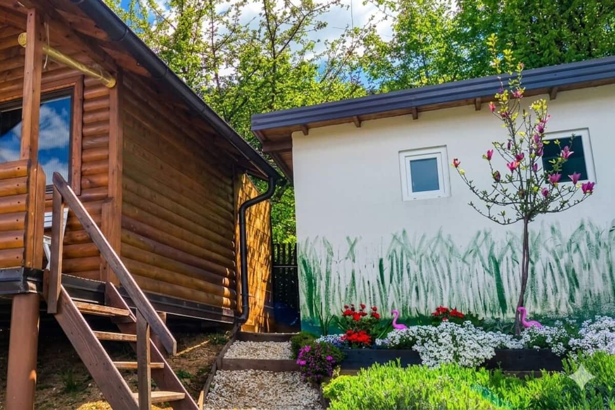 Eine Holzhütte mit einer Veranda, ein kleiner Anbau mit einem Gartenfresko und eine Treppe, die zur Veranda führt.