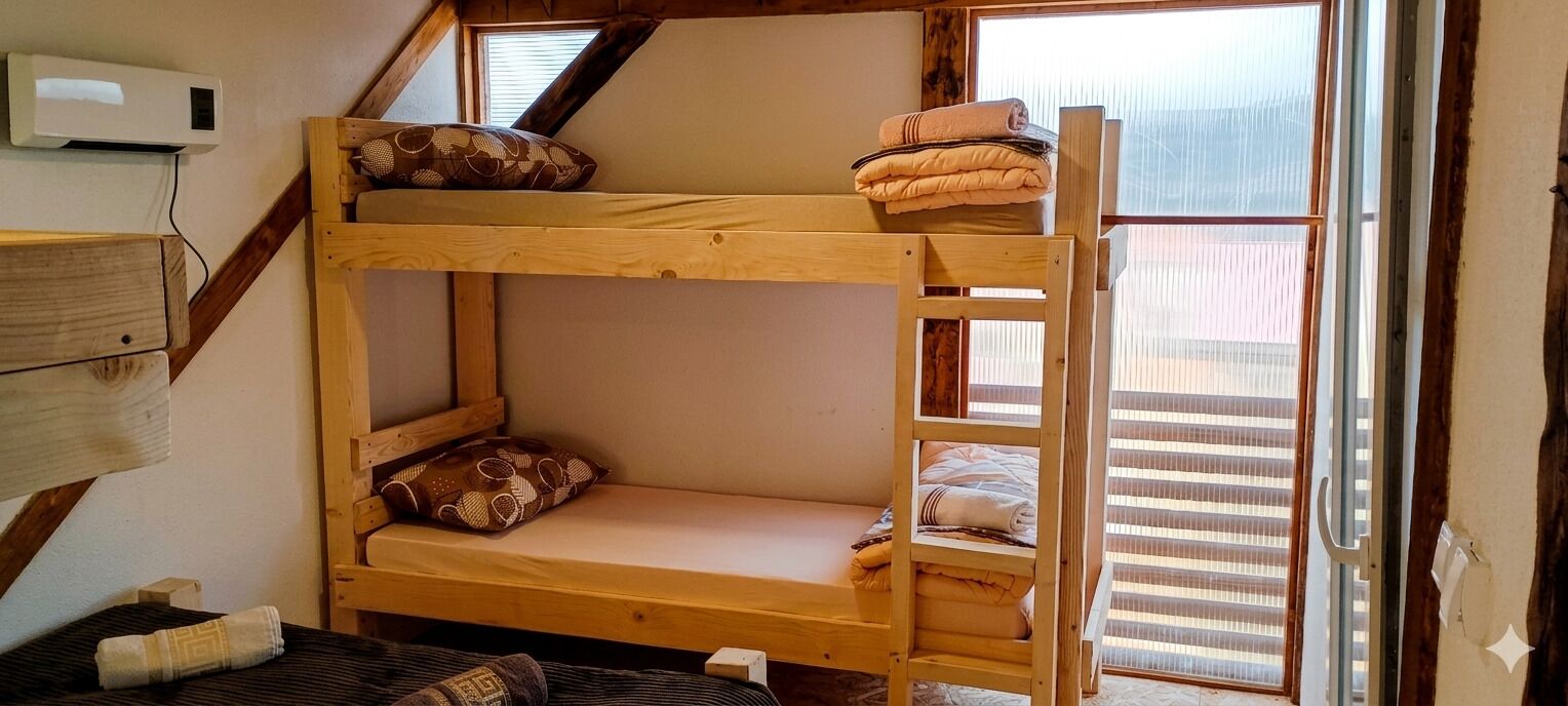 Ein Etagenbett mit Kissen, eine Holzleiter, ein Fenster mit Jalousien und eine Wand-Klimaanlage.
