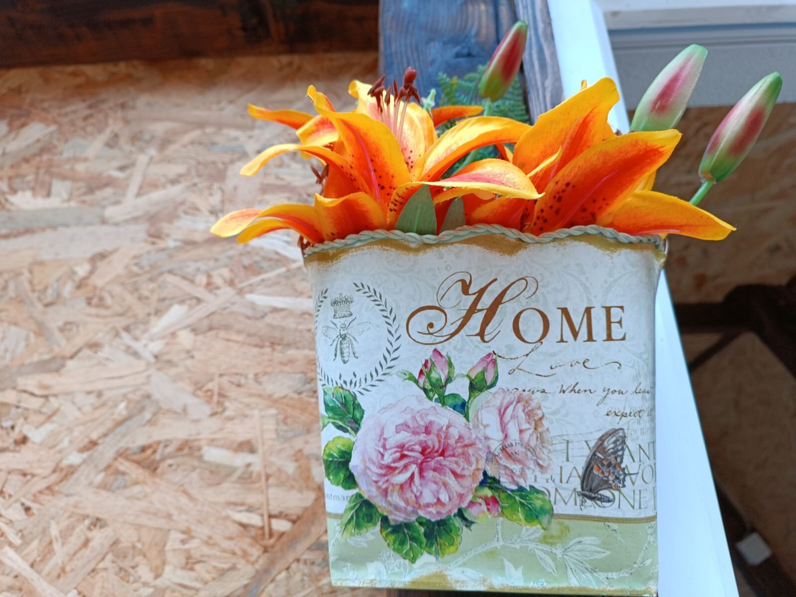 Eine dekorative Vase mit floralem Dekor und dem Schriftzug "HOME", auf einer Holzoberfläche platziert.