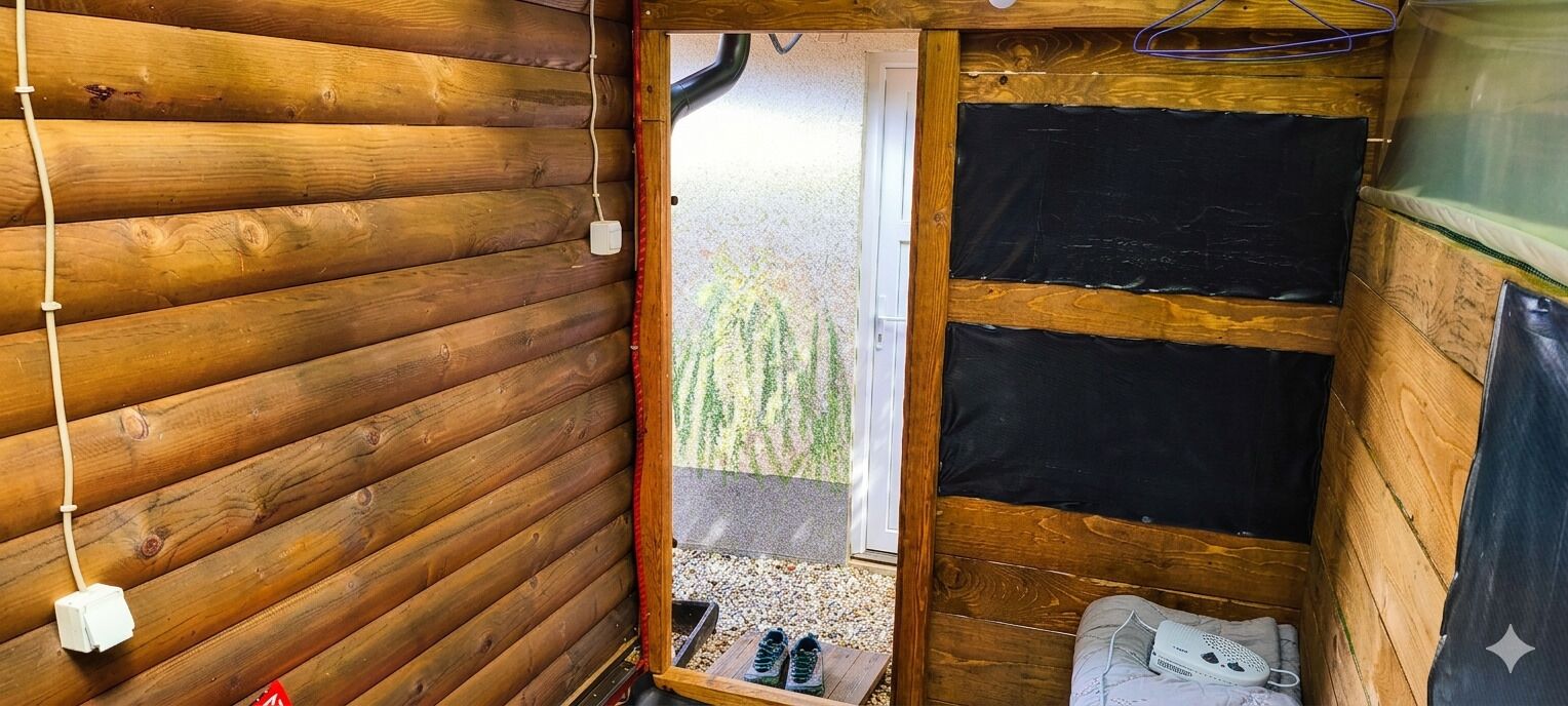 A wooden cabin interior with a door leading outside, a power outlet, and a small table with items on it.