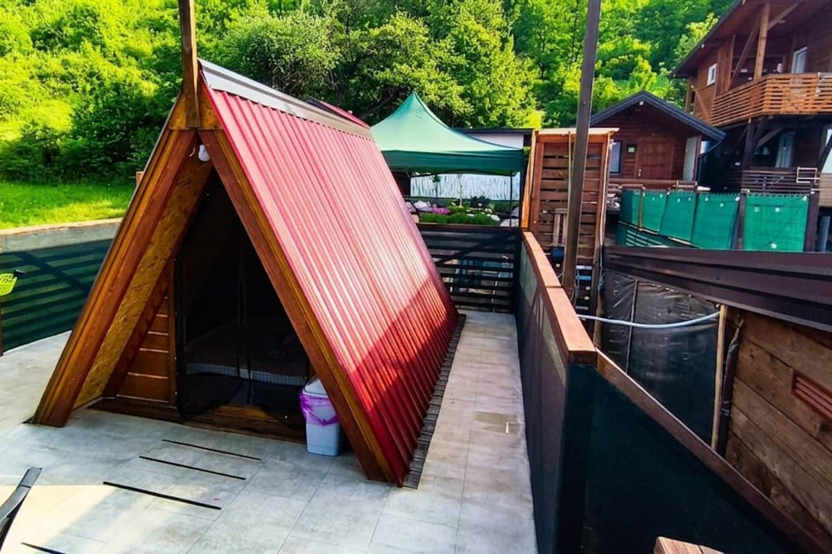 Eine Holzhütte mit geneigtem Dach, einem grünen Zelt und einer Holzterrasse.