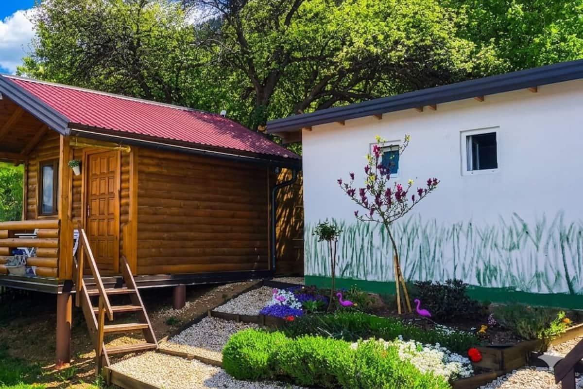 Eine Holzhütte mit rotem Dach, einer kleinen Veranda und einem Garten mit Blumen und Pflanzen.