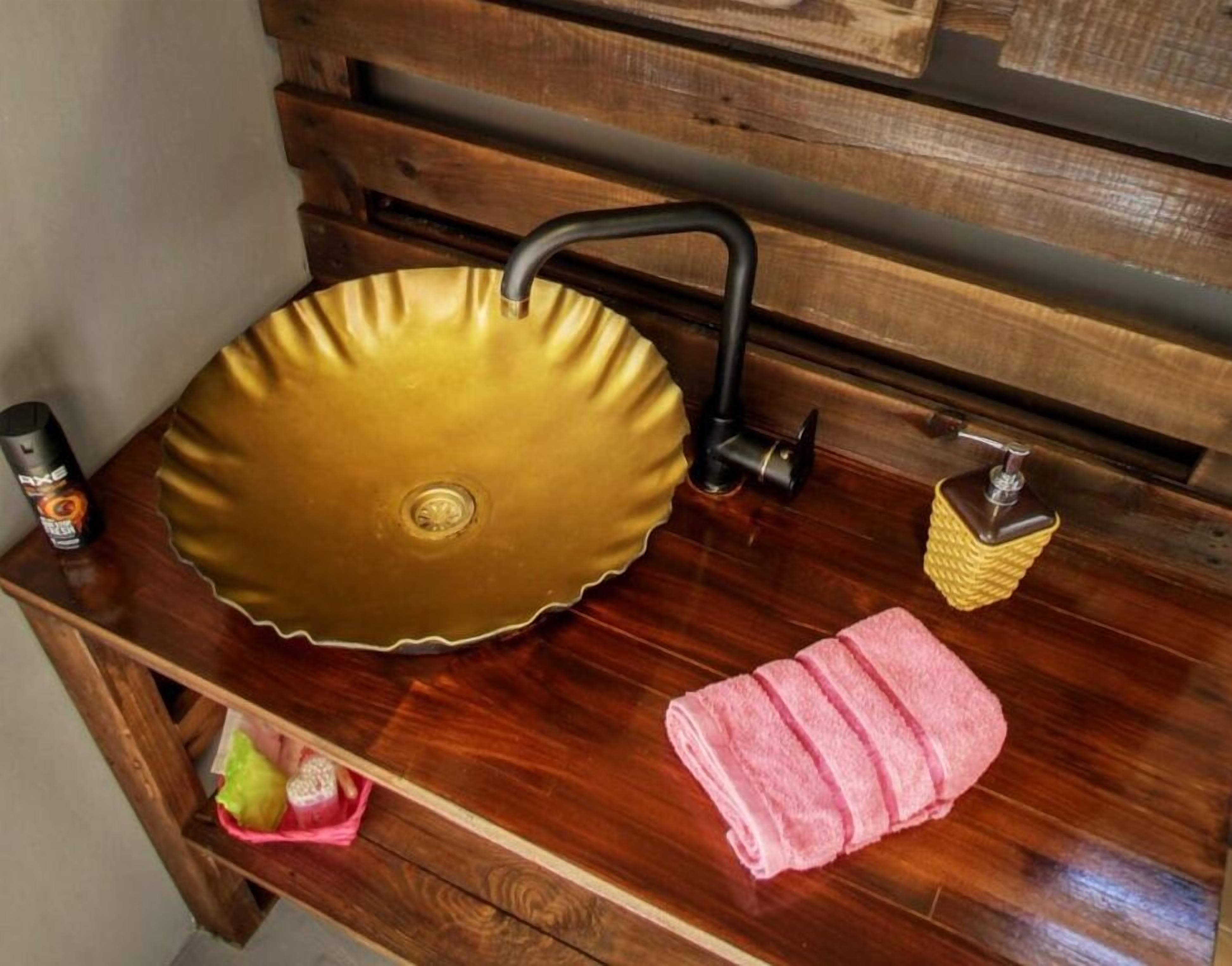Un lavabo da bagno con una vasca dorata, un rubinetto nero, un dispenser di sapone e un asciugamano rosa su un mobile in legno.