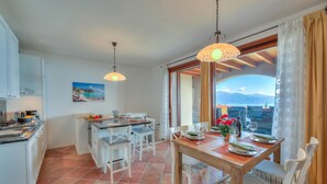 A dining area with a view of the sea, a kitchen with white cabinets, and a dining table set for four.