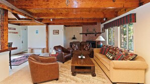 A cozy living room with wooden beams, a fireplace, and a sofa with plaid cushions. - Alpine Skies by Destination Big Bear : Peaceful Setting in Moonridge! Walk to Bear Mtn and the National Forest! Hot Tub! (Big Bear Lake)