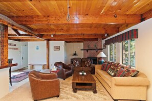 A cozy living room with wooden beams, a fireplace, and a sofa with plaid cushions.