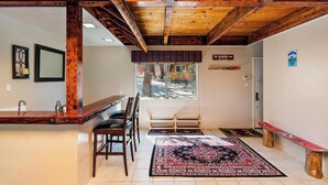 A spacious room with a wooden ceiling, a large window, a bench, and a rug. - Alpine Skies by Destination Big Bear : Peaceful Setting in Moonridge! Walk to Bear Mtn and the National Forest! Hot Tub! (Big Bear Lake)