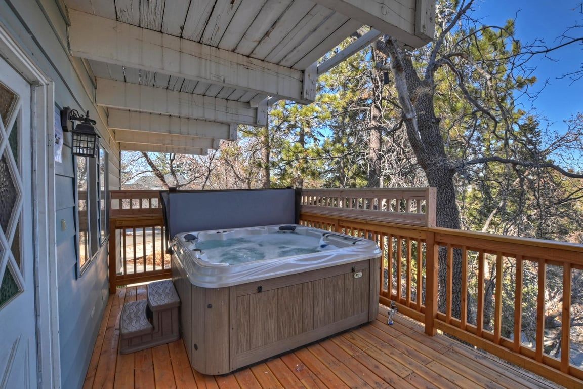 Ein Whirlpool auf einer Holzterrasse mit Holzgeländer und Bäumen im Hintergrund.