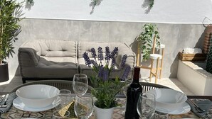 Une table à manger dressée avec de l’assiette blanche, des verres et une bouteille, entourée de plantes en pot et d’un canapé.