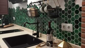 Une cuisine avec un plan de travail noir, un évier, une bouteille de vin et un plateau sur lequel se trouvent un verre et un objet décoratif.