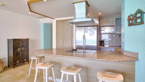 A kitchen with a central island, bar stools, a wooden cabinet, and a decorative house wall art piece.