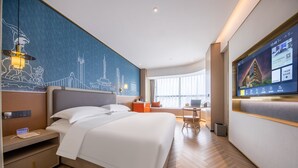 Quarto de hotel moderno com uma cama grande, uma escrivaninha, uma cadeira, uma TV e um mural com vista para a cidade.