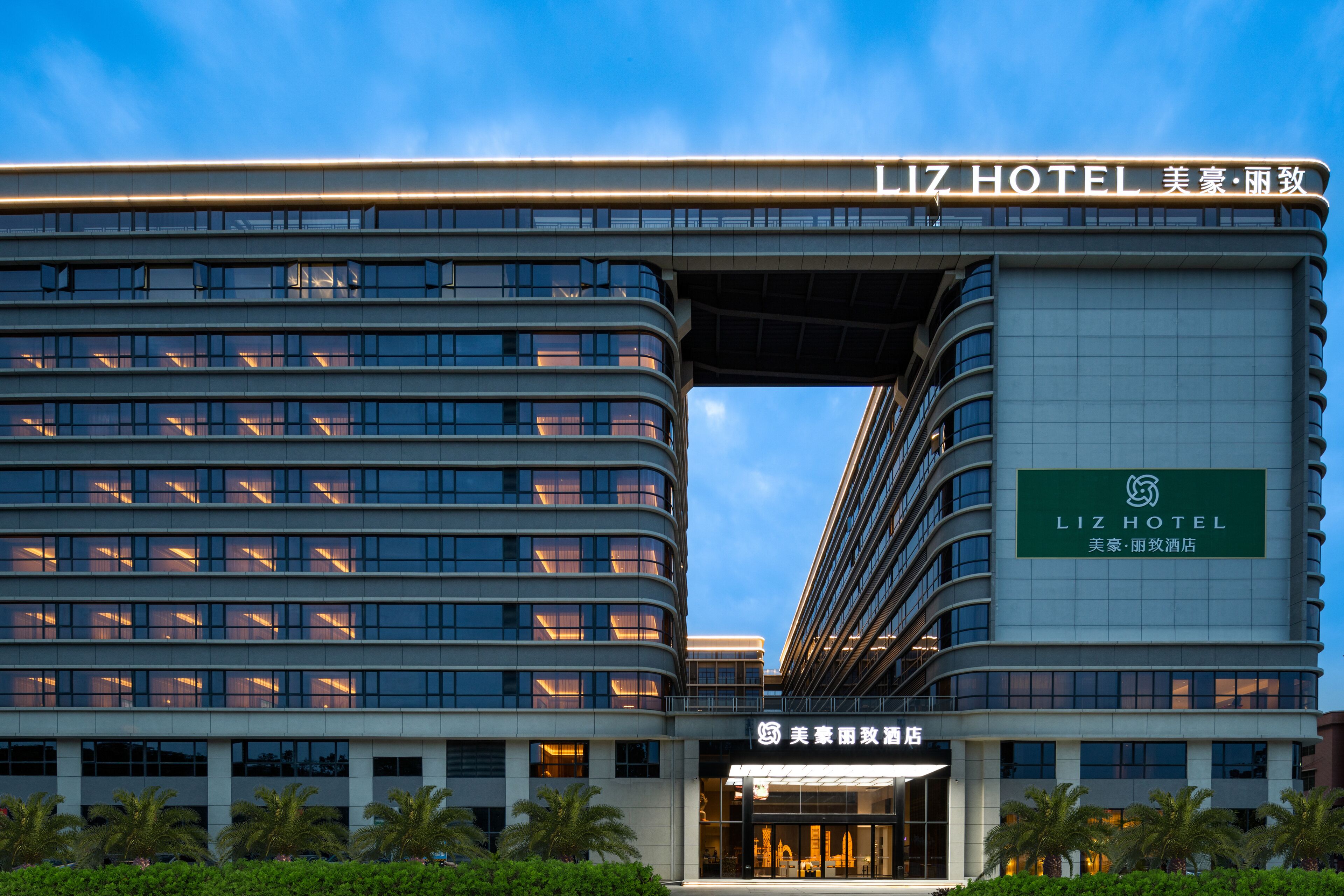 Ein modernes Hotelgebäude mit mehreren Etagen, einem markanten Eingang und Beschilderung, die es als das Liz Hotel kennzeichnet.