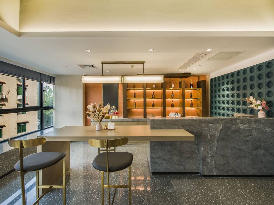 A modern bar area with a marble countertop, two bar stools, and a wall of shelves displaying bottles.
