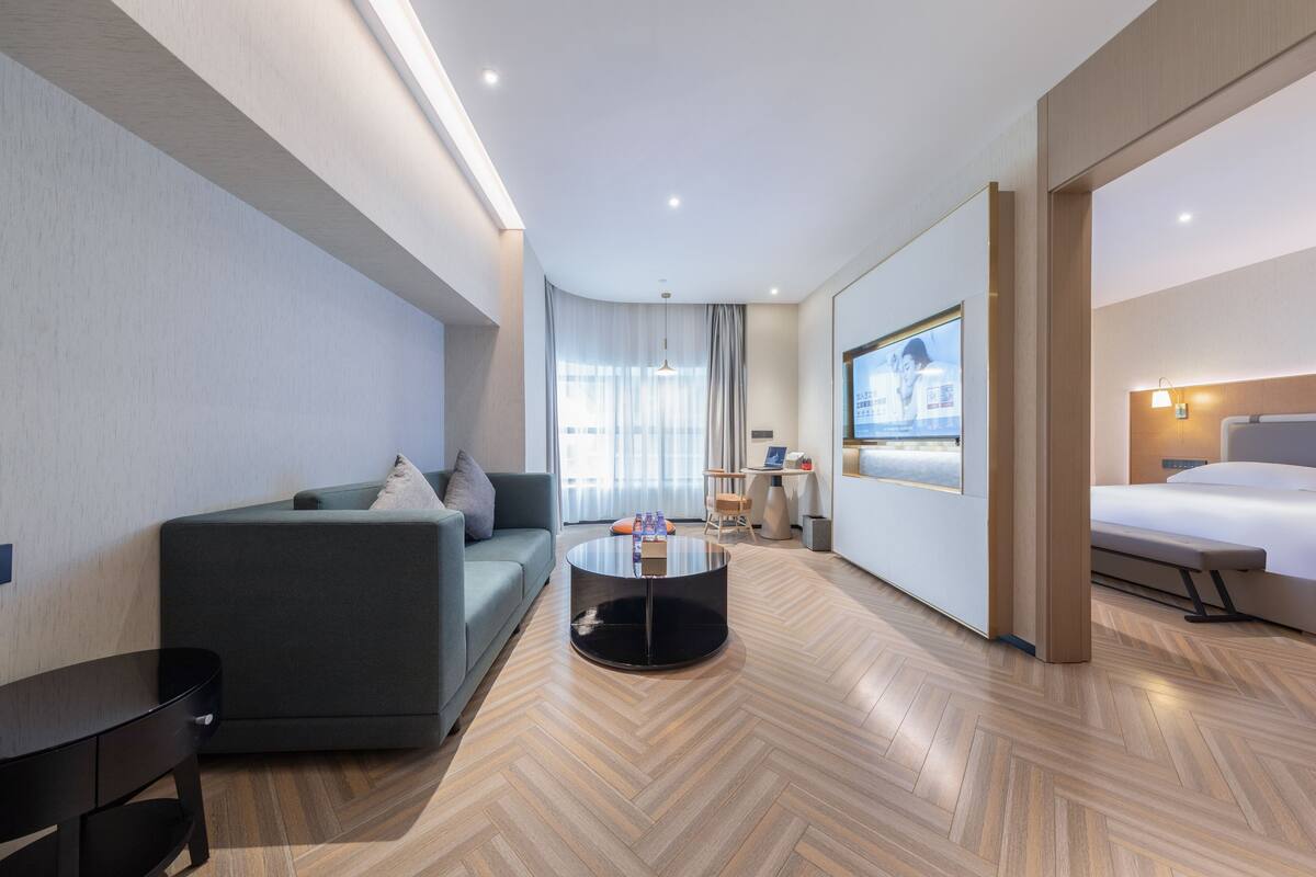 Ett modernt hotellrum med en soffa, ett runt soffbord, en säng och en tv som är monterad på väggen.