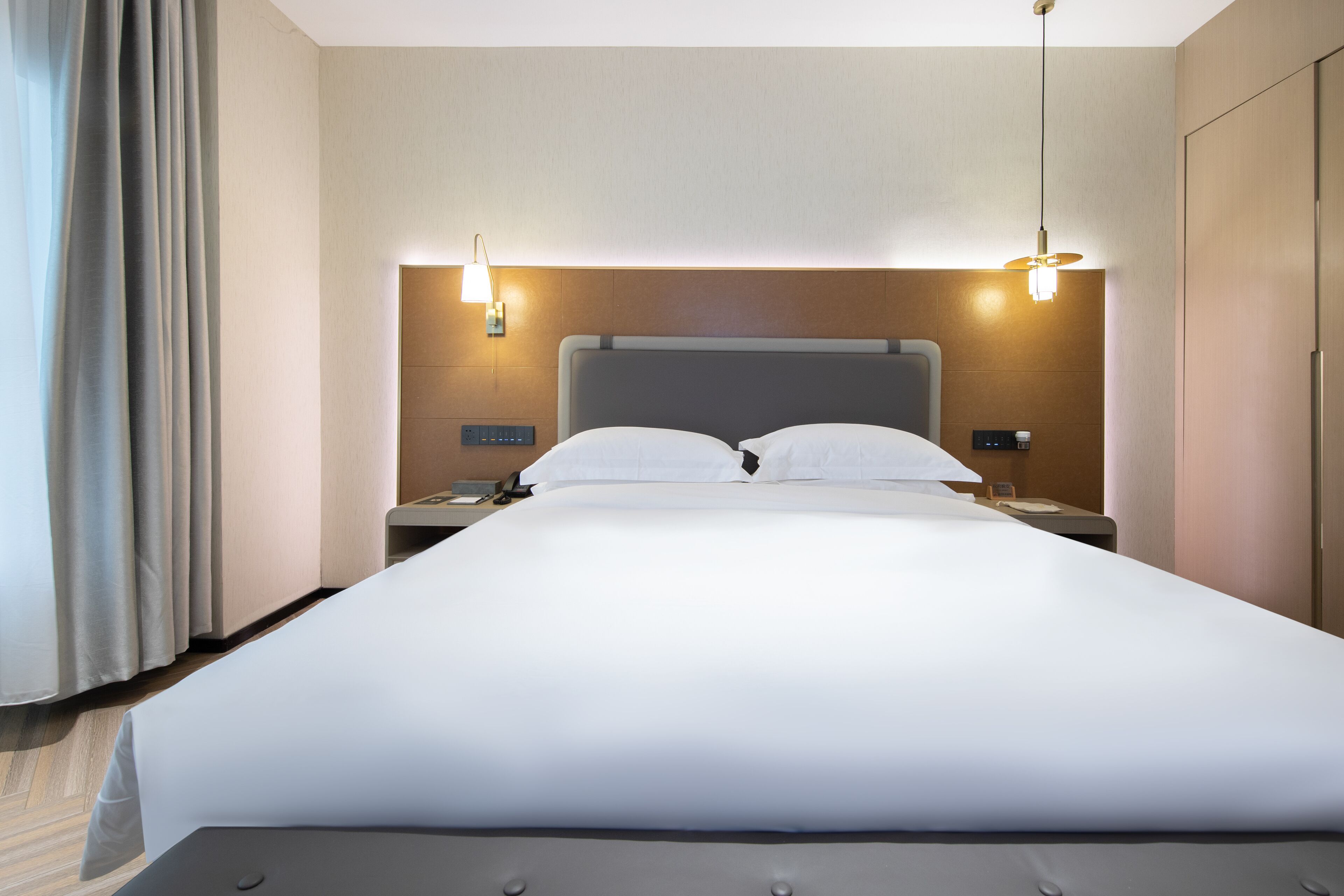 Una habitación de hotel moderna con una cama grande, dos mesitas de noche y un cabecero con iluminación integrada.