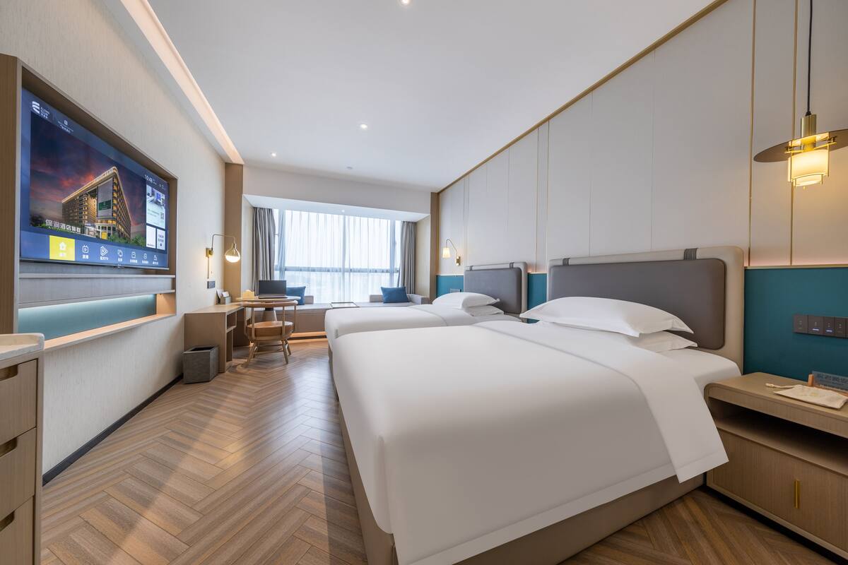 Ett hotellrum med två sängar, ett skrivbord, en TV och ett fönster.