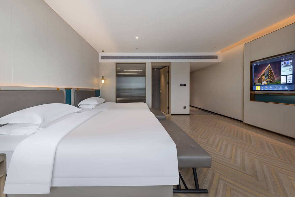 Ett modernt hotellrum med en stor säng, en platt-TV som är monterad på väggen och ett trägolv med fiskbensmönster.