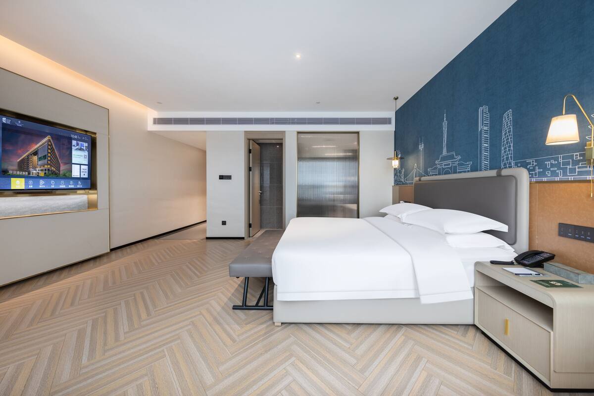 Ett modernt hotellrum med en stor säng, ett skrivbord, en TV och en väggmålning som föreställer en stadsbild.